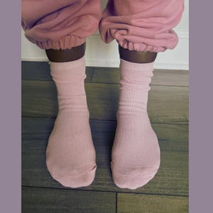 Puede incluir: Un par de calcetines de canal&eacute; rosa claro se llevan con un pantal&oacute;n de ch&aacute;ndal rosa a juego. Los calcetines est&aacute;n subidos, con la tela recogida alrededor de los tobillos. El fondo es un suelo de madera.