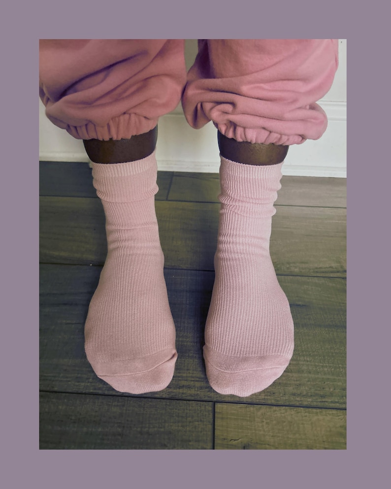 Puede incluir: Un par de calcetines de canal&eacute; rosa claro se llevan con un pantal&oacute;n de ch&aacute;ndal rosa a juego. Los calcetines est&aacute;n subidos, con la tela recogida alrededor de los tobillos. El fondo es un suelo de madera.