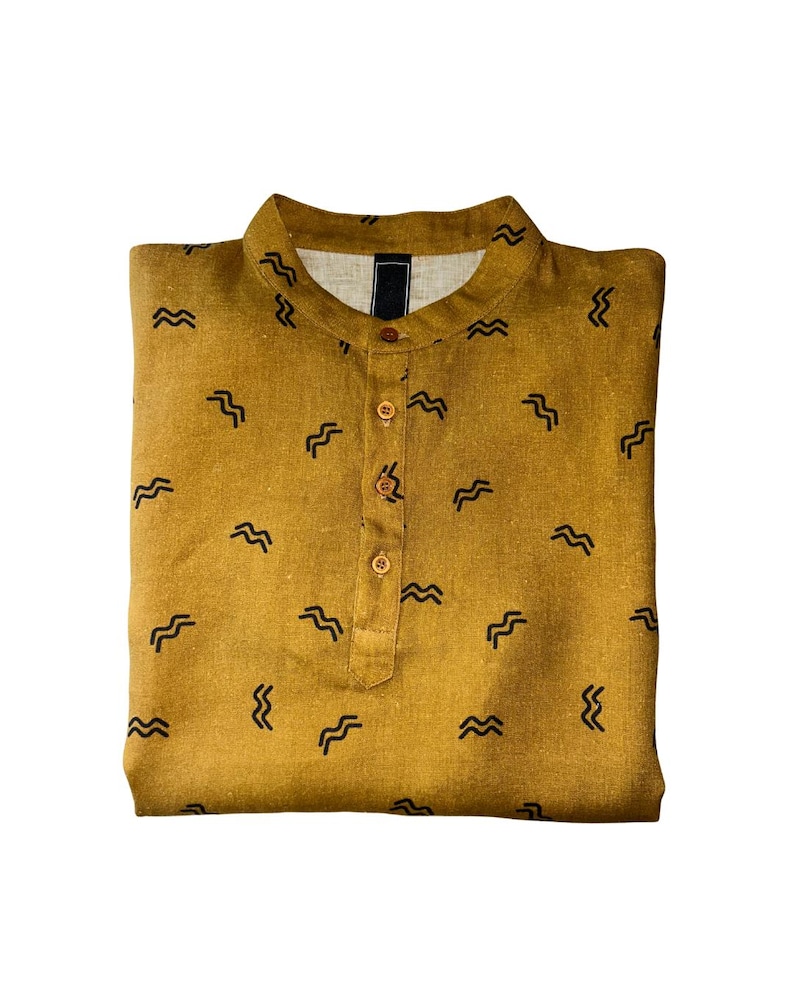 May include: Mustard-colored shirt with a mandarin collar and a button-down placket. The shirt is patterned with small, black, wave-like designs. The shirt is folded neatly, showcasing its design and construction. A casual, everyday garment.