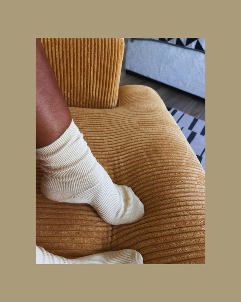 Puede incluir: Calcetines acanalados color crema sobre una silla de pana amarillo mostaza. Los calcetines est&aacute;n doblados en la parte superior y cubren el pie y el tobillo. La silla tiene una superficie texturizada.