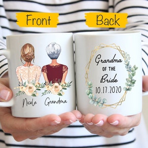 Pode incluir: Caneca de cer&acirc;mica branca com um desenho de duas mulheres, uma com cabelo castanho e outra com cabelo grisalho, com o texto "Nicole Grandma" na frente. A parte de tr&aacute;s da caneca tem uma moldura geom&eacute;trica dourada com folhas verdes e o texto "Grandma of the Bride 10.17.2020".
