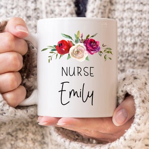 Puede incluir: Taza de cer&aacute;mica blanca con un dise&ntilde;o floral con flores rojas, rosas y blancas. La taza tiene el texto "NURSE Emily" impreso en ella.