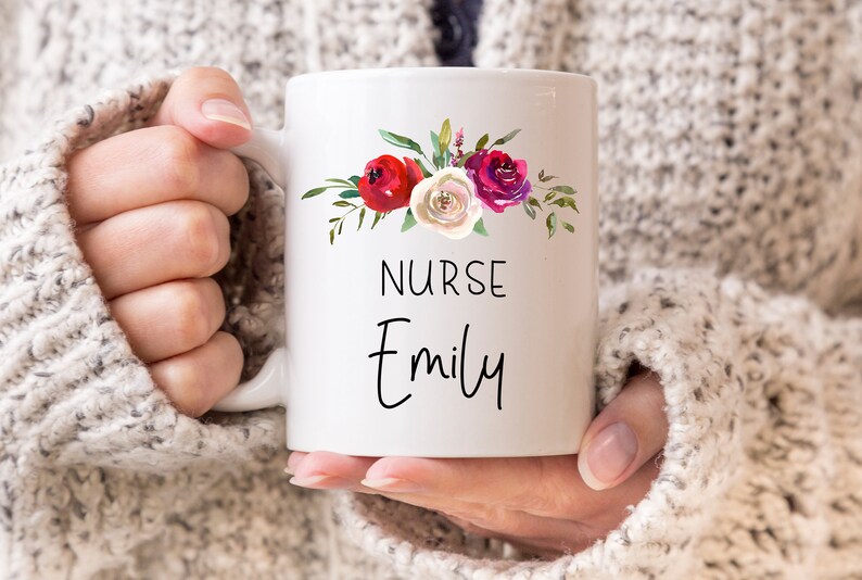 Puede incluir: Taza de cer&aacute;mica blanca con un dise&ntilde;o floral con flores rojas, rosas y blancas. La taza tiene el texto "NURSE Emily" impreso en ella.