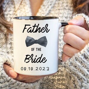 May include: White ceramic mug with a black rim and handle. The mug has black text that reads "Father of the Bride" with a black bow tie graphic and the date "08.18.2023".