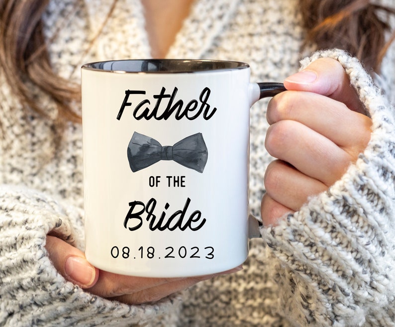 May include: White ceramic mug with a black rim and handle. The mug has black text that reads "Father of the Bride" with a black bow tie graphic and the date "08.18.2023".