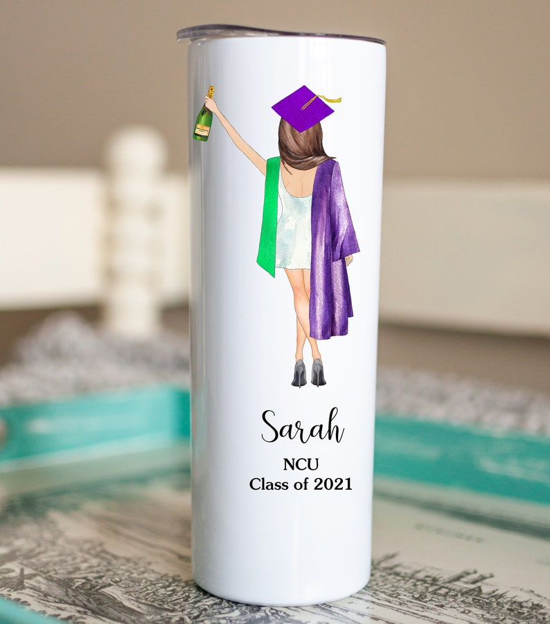 K&ouml;nnte beinhalten: Ein wei&szlig;er Edelstahlbecher mit einer Illustration von einer violetten und gr&uuml;nen Abschluss-Kappe und -Robe. Der Text "Sarah NCU Class of 2021" ist auf dem Becher aufgedruckt.