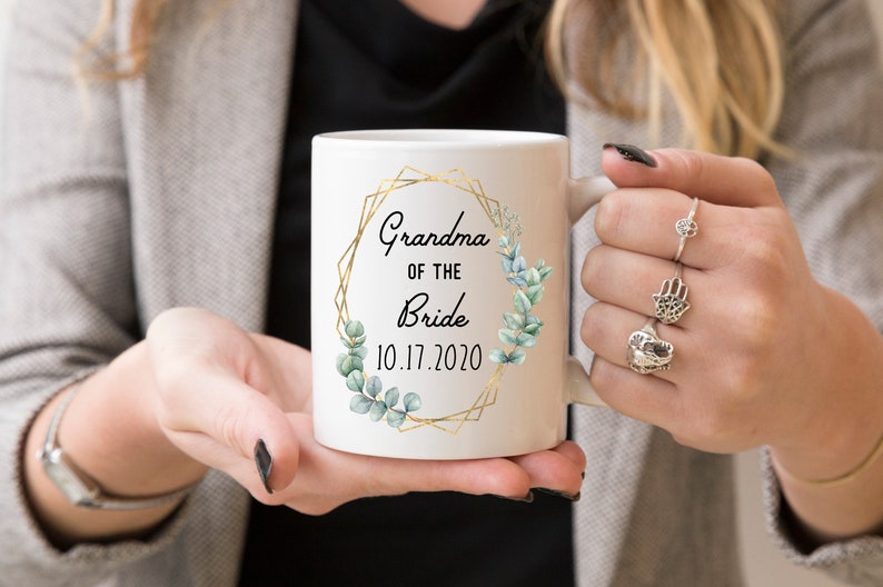 Pode incluir: Caneca de cer&acirc;mica branca com moldura geom&eacute;trica dourada e folhas de eucalipto verdes. O texto diz "Grandma of the Bride 10.17.2020".