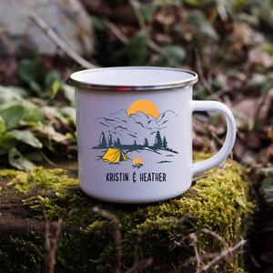 May include: White enamel camping mug with a mountain scene and a yellow tent. The mug has the text "Kristin & Heather" printed on the bottom.