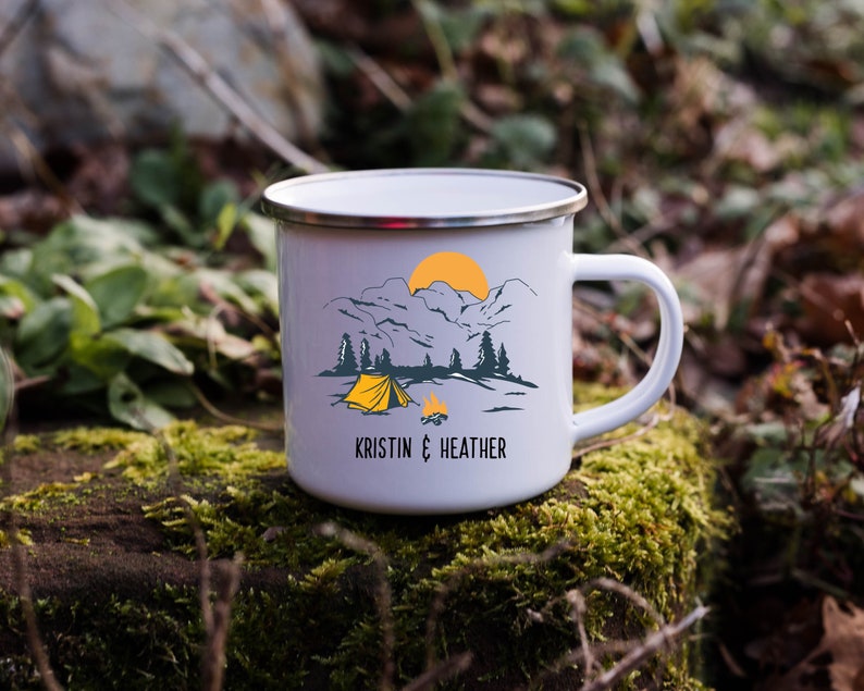 May include: White enamel camping mug with a mountain scene and a yellow tent. The mug has the text "Kristin & Heather" printed on the bottom.