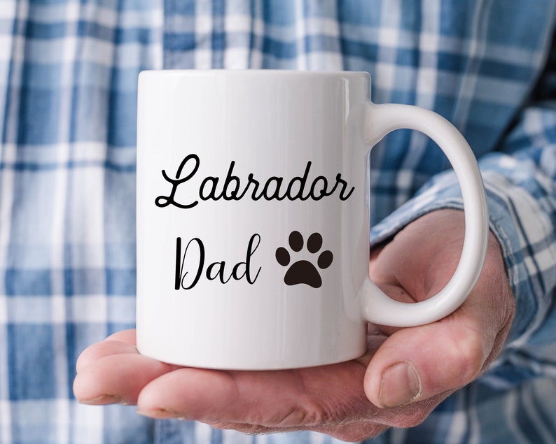 Puede incluir: Taza de cer&aacute;mica blanca con las palabras "Labrador Dad" en escritura negra y una huella de pata negra. La taza tiene un asa curvada.