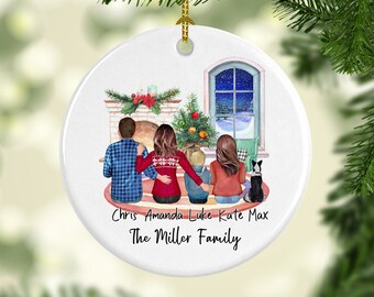 May include: A white ceramic Christmas ornament featuring a family of four and a dog sitting in front of a fireplace. The ornament has a snowy winter scene in the background and the text "Chris Amanda Luke Kate Max The Miller Family".