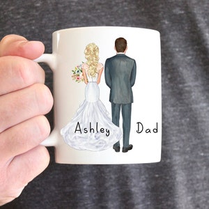 May include: White ceramic mug with a hand-drawn illustration of a bride and groom in wedding attire. The bride is holding a bouquet of flowers. The text "Ashley" and "Dad" is written below the couple.