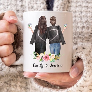 K&ouml;nnte beinhalten: Wei&szlig;e Keramiktasse mit einer Aquarell-Illustration von zwei Frauen in schwarzen Jacken, die Kaffeetassen halten. Die Frauen stehen R&uuml;cken an R&uuml;cken mit einem floralen Design am Boden der Tasse. Der Text "Emily & Jessica" ist unter dem Design gedruckt.
