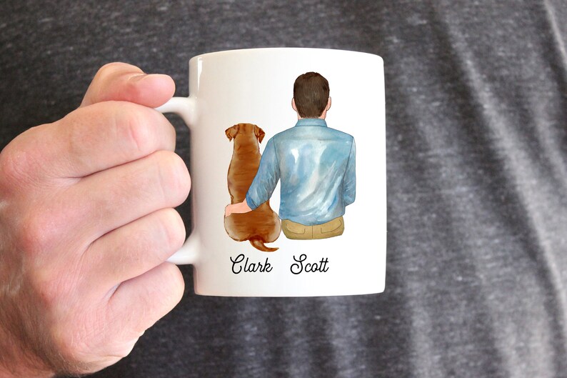 Puede incluir: Taza de cer&aacute;mica blanca con una ilustraci&oacute;n a la acuarela de una persona y un perro. La persona lleva una camisa azul y pantalones color caqui, con el perro a su lado. Los nombres "Clark Scott" est&aacute;n impresos debajo.