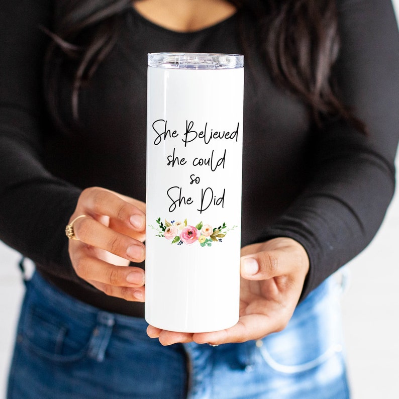 K&ouml;nnte beinhalten: Ein wei&szlig;er Becher mit einem Blumenmuster und dem Text "She Believed she could so She Did."