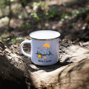 May include: White enamel camping mug with a mountain scene and a yellow tent. The mug has a silver rim and the text "Kristin & Heather" printed on the bottom.