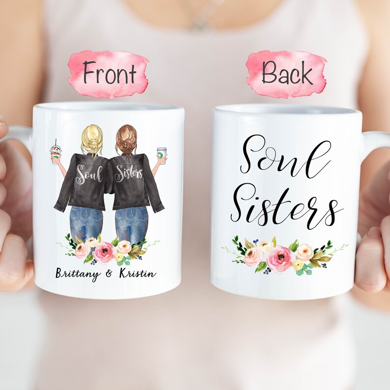 May include: White ceramic mug featuring a graphic of two figures in black jackets and jeans, holding coffee cups. The front of the mug says "Soul Sisters" and the names "Brittany & Kristin". Floral accents adorn the bottom.