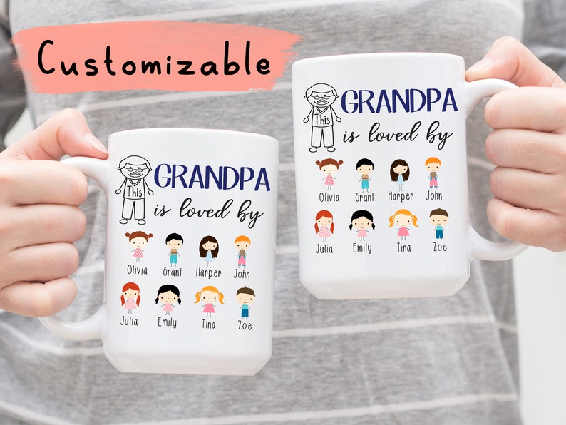 May include: White ceramic mug with a blue inscription that reads "GRANDPA is loved by". The mug features a cartoon drawing of a man with a beard and the word "This" written on his shirt. Below the inscription are eight cartoon drawings of children with their names printed below each drawing. The names are Olivia, Grant, Harper, John, Julia, Emily, Tina, and Zoe.