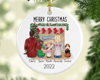 May include: White ceramic Christmas ornament with a family of four standing in front of a fireplace. The ornament has the text "Merry Christmas" at the top and "Chris Rosie Noah Amanda Tucker 2022" at the bottom.