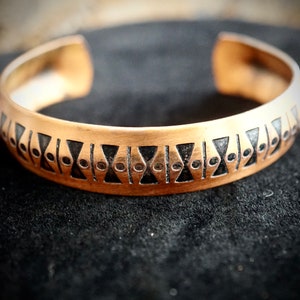 May include: A copper bracelet with a geometric pattern of black triangles and circles.