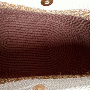 K&ouml;nnte beinhalten: Nahaufnahme des Inneren einer wei&szlig;en und braunen gewebten Tragetasche. Die Tasche hat ein braunes gewebtes Futter und einen goldenen Metallknopf.