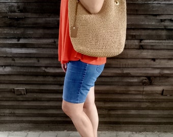 May include: A woman wearing a red shirt and denim shorts is carrying a large, brown, woven tote bag with a leather strap and gold hardware.