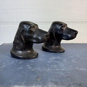May include: A pair of black, dog-shaped salt and pepper shakers. Each shaker is sculpted in the likeness of a hound dog head with long, drooping ears, a smooth finish, and small holes on the top of the head for dispensing seasoning.