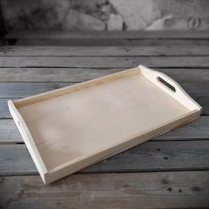 Op de afbeelding: Een dienblad van naturel hout met twee handvatten. Het dienblad is rechthoekig en heeft een lichte houtkleur.