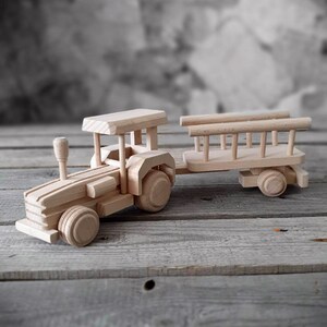 Op de afbeelding: Een houten speelgoedtractor met een aanhanger. De tractor heeft een cabine, wielen en een stuurwiel. De aanhanger heeft een houten frame en is aan de tractor bevestigd.