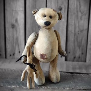 Peut inclure: Un ours en peluche de style vintage et une petite poupée lapin. L'ours est beige avec un nez noir et un patch cousu sur la poitrine. Le lapin est brun clair et tenu par un ruban noir. Les jouets ont un aspect usé et antique.