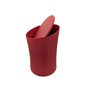 Puede incluir: Un cubo de basura rojo con tapa a juego. El cubo tiene una textura acanalada y una forma curva. La tapa está parcialmente abierta, revelando el interior. El diseño es moderno y minimalista.