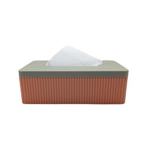Op de afbeelding: Een rechthoekige tissuebox met een lichtgrijze bovenkant en een koraalkleurige, verticaal geribbelde behuizing. Witte tissues zijn zichtbaar, die uit de opening aan de bovenkant komen. Het ontwerp is modern en minimalistisch.