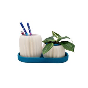 Könnte beinhalten: Ein cremefarbenes Schreibtisch-Organizer-Set mit geripptem Design. Das Set enthält einen Stifthalter mit Stiften und eine kleine Topfpflanze, die alle auf einem türkisfarbenen Tablett liegen. Die Pflanze hat grüne Blätter. Der Stifthalter ist etwa 10 cm hoch.