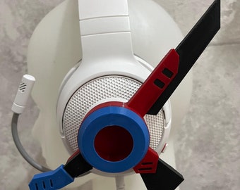 May include: A white gaming headset with a blue, red, and black stand. The stand has a circular design with a hole in the center.