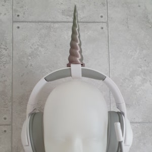 May include: White headphones with a gray earcup and a pink and green unicorn horn attached to the top.