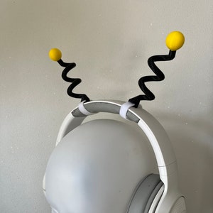 May include: White headphones with a black headband and yellow antennae. The antennae are made of a flexible, springy material.