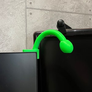 May include: A bright green plastic monitor stand with a curved arm and a round head. The stand is attached to the top of a black computer monitor.