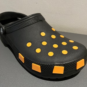 Könnte beinhalten: Schwarzer Clog mit gelbem Punktmuster und gelben quadratischen Akzenten an der Sohle.