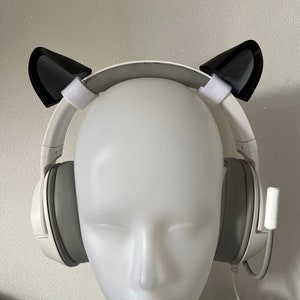 May include: White wireless headphones with black cat ears attached to the headband. The headphones are on a white mannequin head.