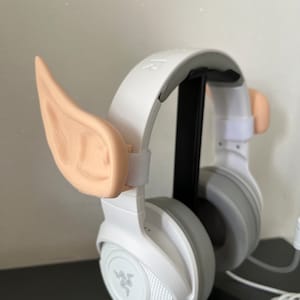 May include: White Razer headphones with a black stand and two beige elf ears attached to the headband.