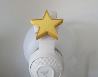 Può includere: Cuffie bianche con un accessorio a forma di stella gialla attaccato alla parte superiore.
