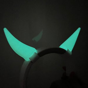May include: A pair of glow-in-the-dark devil horns headband. The horns are a bright green colour and are attached to a white headband.