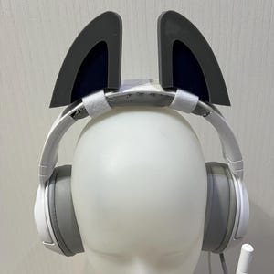 May include: White headphones with grey earcups and a microphone. The headphones have grey cat ears attached to the headband.