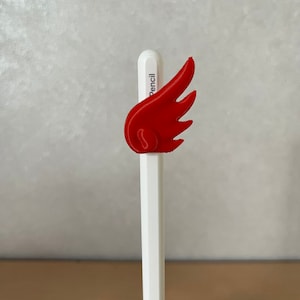 Op de afbeelding: Een wit potlood met een rode plastic vleugelvormige topper. De topper is een 3D-geprint ontwerp.