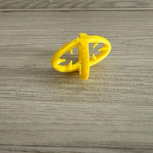 Può includere: Un oggetto giallo brillante stampato in 3D composto da due anelli intersecanti con piccole punte rivolte verso l'interno dai bordi delle cornici circolari, creando una struttura geometrica simile a una gabbia con una superficie testurizzata.