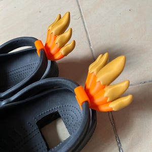 Può includere: Un paio di zoccoli neri con ciondoli per scarpe a forma di fiamma arancioni e gialli attaccati alle cinghie posteriori.