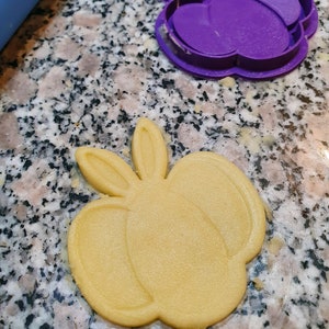 May include: A yellow cookie in the shape of a bunny rabbit with long ears, cut out using a purple plastic cookie cutter.