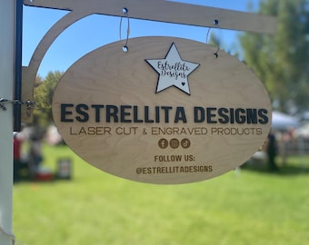 May include: A wooden sign with the text "Estrellita Designs" and "Laser Cut & Engraved Products". The sign also includes social media icons for Facebook, Instagram, and TikTok, and the text "Follow Us: @EstrellitaDesigns".