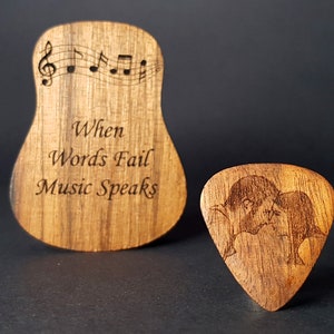 May include: A wooden guitar pick with a couple kissing engraved on it. A larger wooden guitar shaped sign with the text "When Words Fail Music Speaks" and musical notes is also shown.