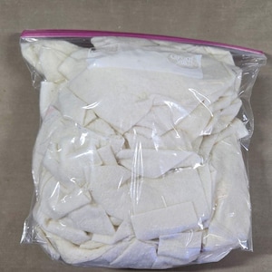 May include: A clear plastic bag filled with off-white fabric scraps. The bag has a pink zipper closure and a white label that reads "Great Value". The fabric pieces are various shapes and sizes.